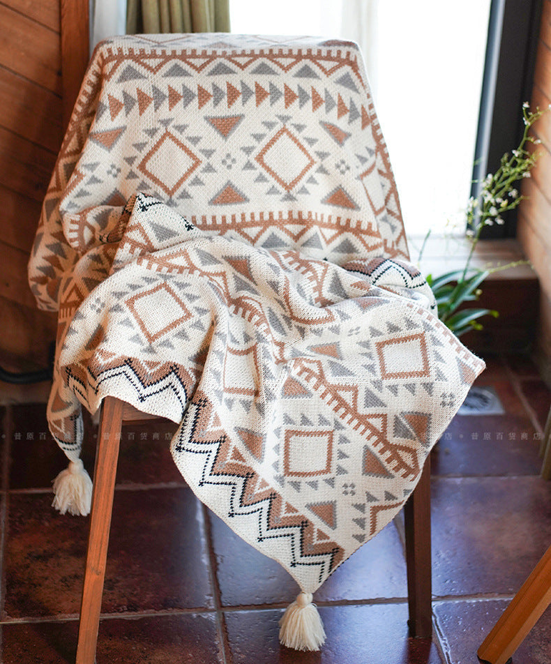 Two patterned blankets draped over a chair with a wooden floor and plant in the background.