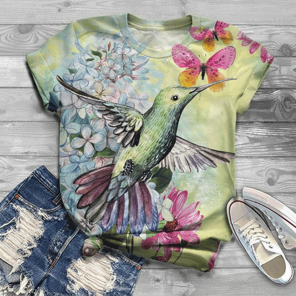 T-shirt with a hummingbird and floral design on a wooden surface with jeans and shoes.