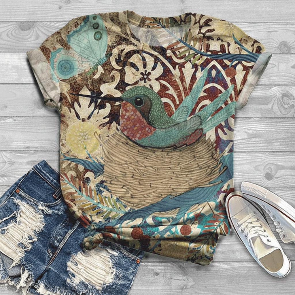Colorful t-shirt with a bird design on a wooden surface with jeans and shoes.