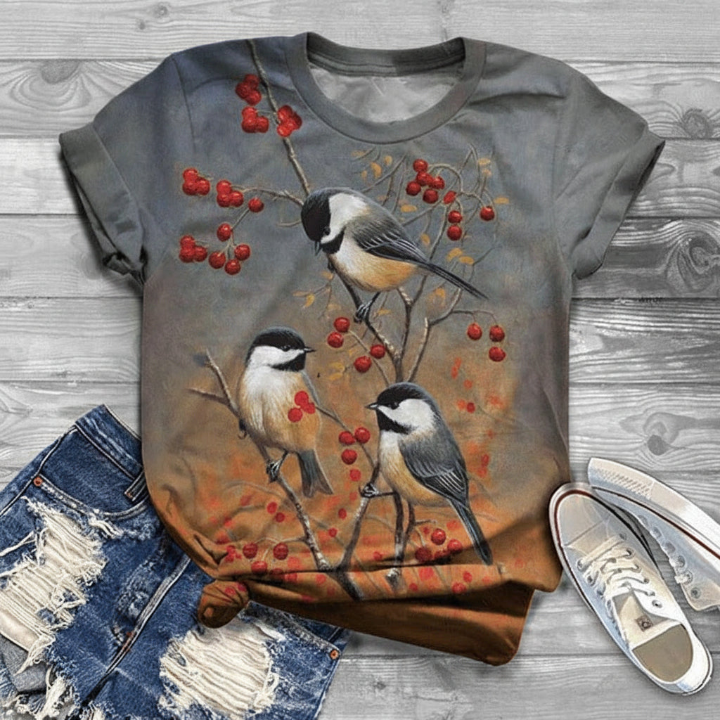 Gray t-shirt with bird and berry design on a wooden surface with jeans and shoes.