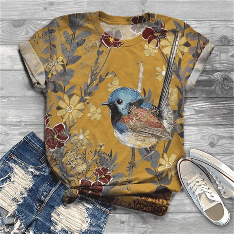 Yellow t-shirt with bird and floral design on a wooden surface with jeans and sneakers.