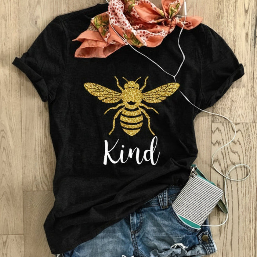 Black t-shirt with bee design and 'Kind' text, paired with denim shorts on a wooden surface.