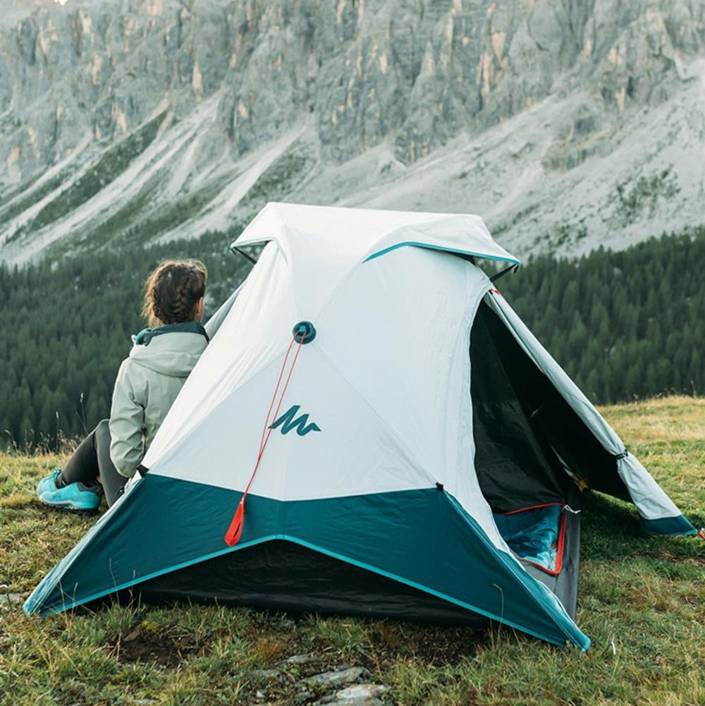 Camping scene with a tent, person sitting outside, and mountain landscape.