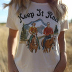 Person wearing a t-shirt with a graphic of two people on horses and the text 'Keep It Rad' in a field.