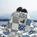 Two people sitting together under a patterned blanket with dog designs by a lake.