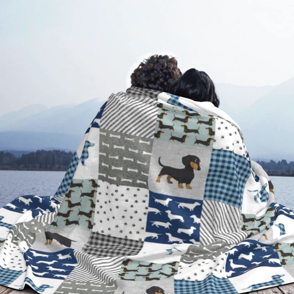 Two people sitting together under a patterned blanket with dog designs by a lake.
