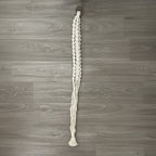 Knotted white macrame plant hanger on a wooden surface.