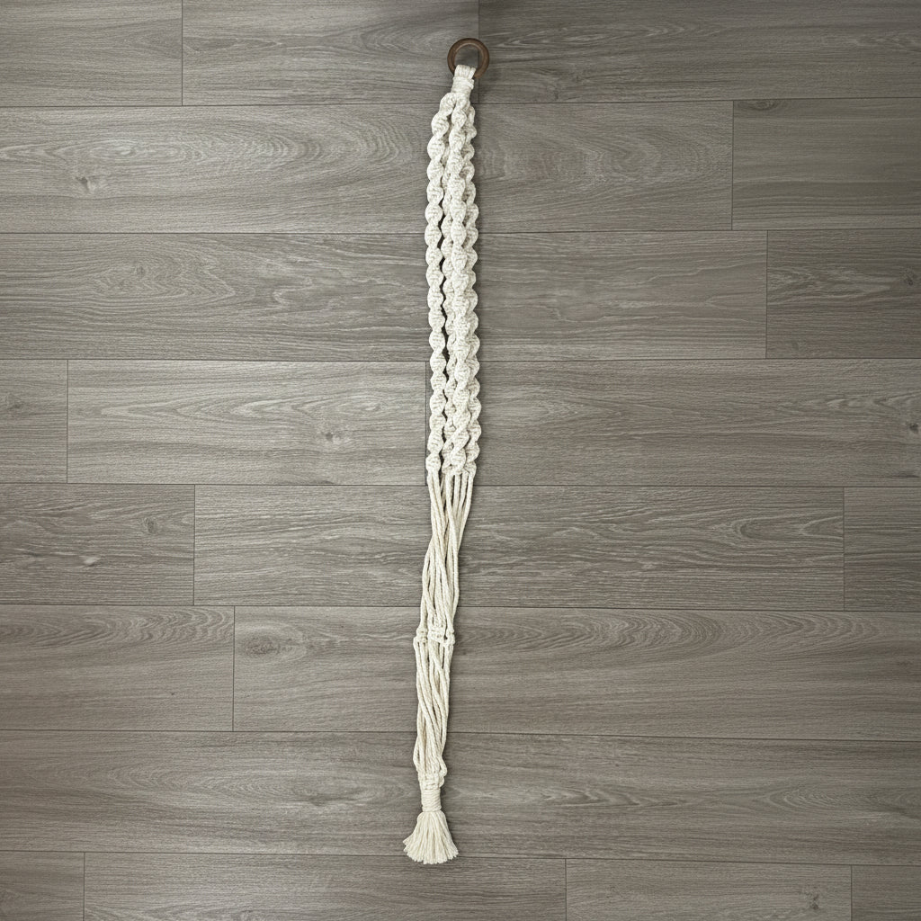 Knotted white macrame plant hanger on a wooden surface.
