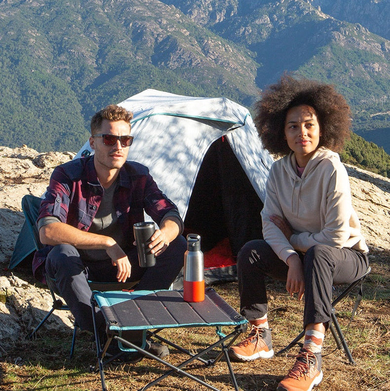 Two people sitting in front of a tent with mountains in the background