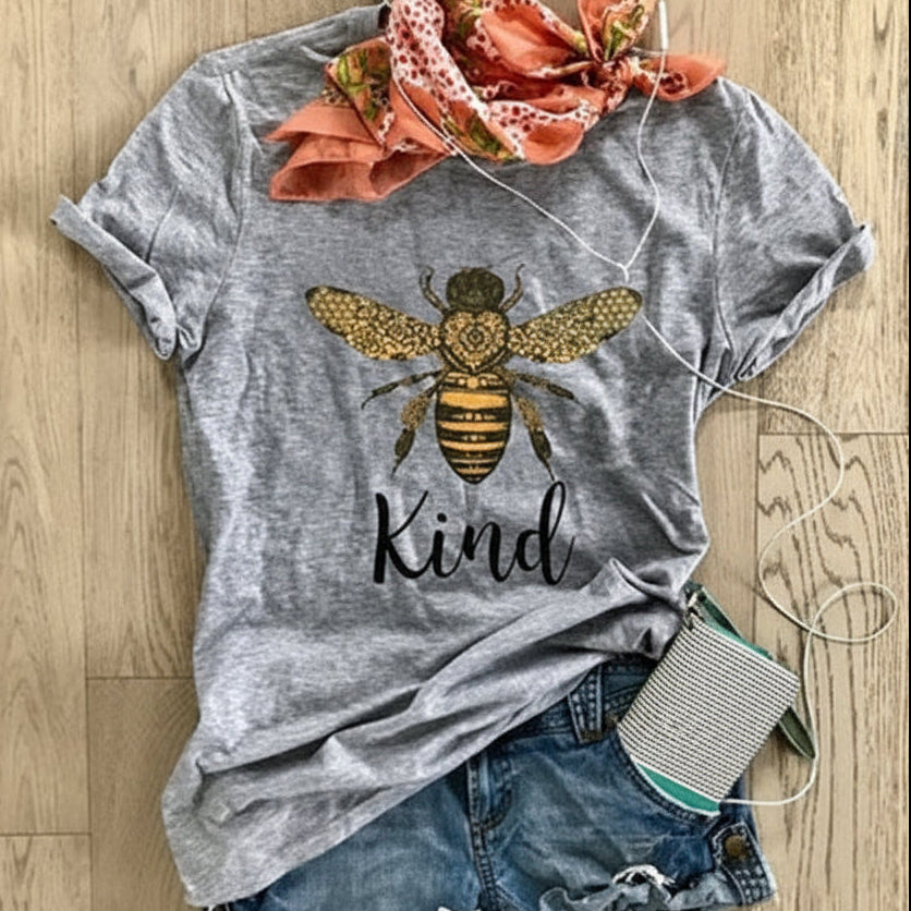 Gray t-shirt with bee and 'Kind' text design, paired with denim shorts and a floral headscarf on a wooden surface.