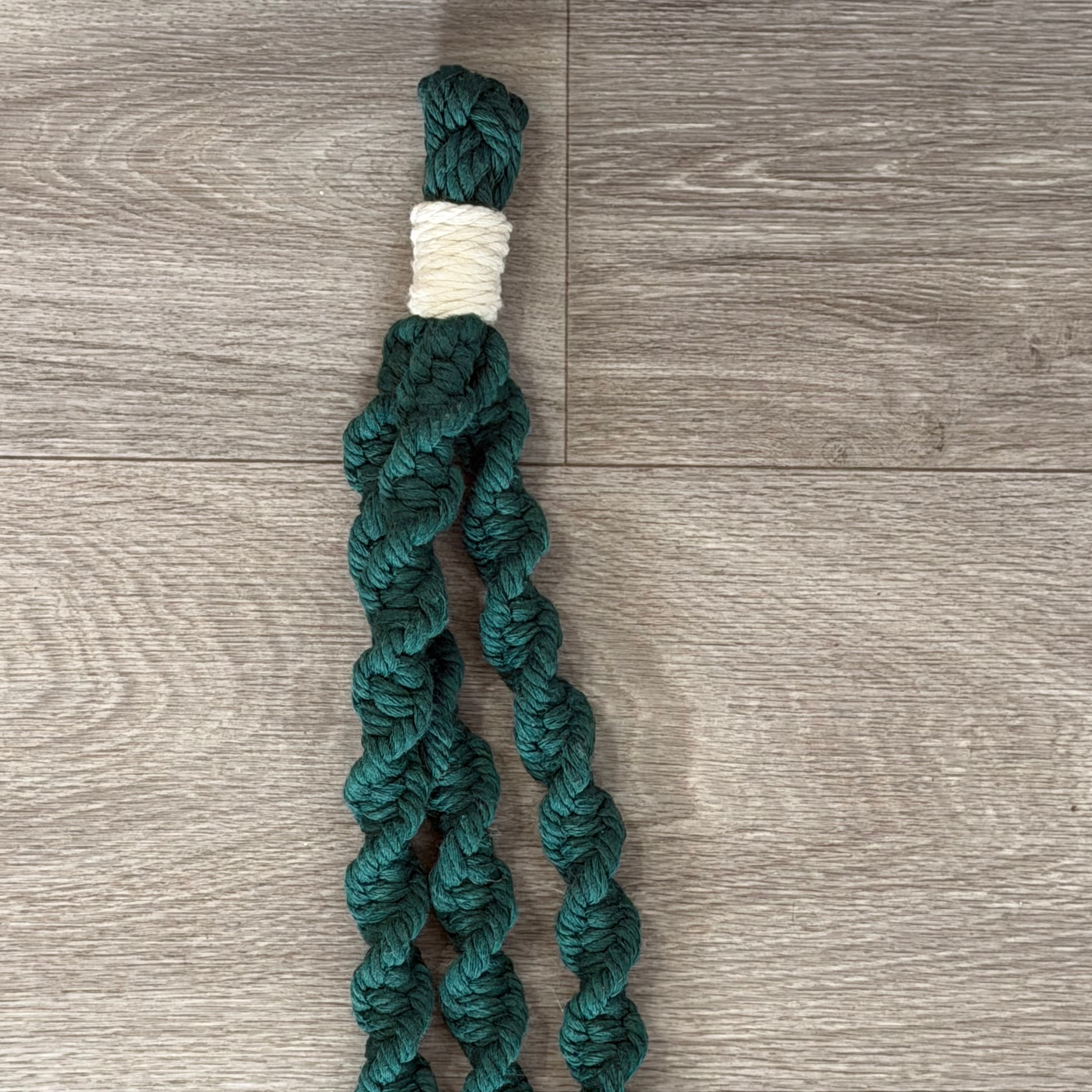 Close up of top of forest green twisted macrame plant hanger with off white accents.