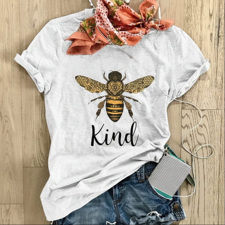 White t-shirt with bee and 'Kind' graphic on a wooden surface